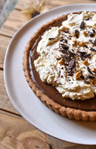 Chocolate Cinnamon Espresso Tart garnished with fresh whipped cream shaved chocolate and crushed peanuts on a white plate and wood background