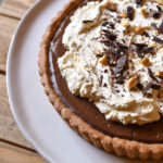 Chocolate Cinnamon Espresso Tart garnished with fresh whipped cream shaved chocolate and crushed peanuts on a white plate and wood background