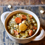 A bowl of Verde Pozole in a white bowl with hominy garnish on a slate background