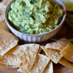 A bowl of Green Onion Guacamole surrounded by chips garnished with a lime