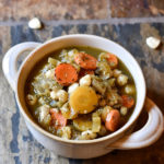 A bowl of Verde Pozole in a white bowl with hominy garnish on a slate background