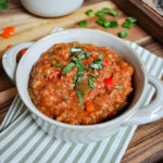 A bowl of Vegetable Stuffed Red Pepper Soup on a green stripped napkin and wood tray.