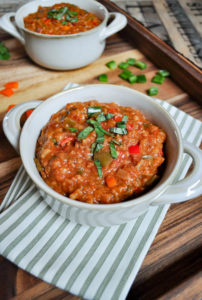 A bowl of Vegetable Stuffed Red Pepper Soup on a green stripped napkin and wood tray.