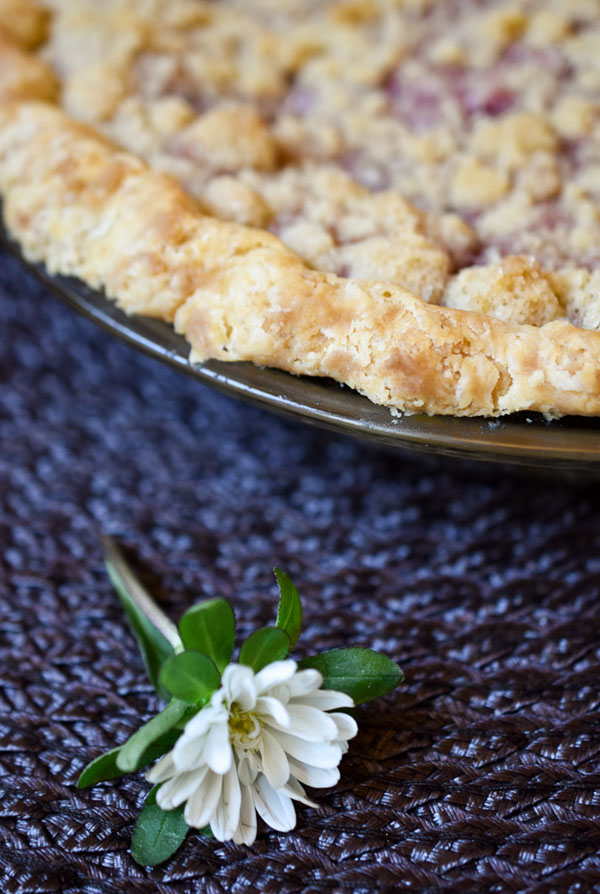 A blackberry orange mint pie on a placemat garnished with a white flower