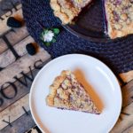 slice of blackberry orange mint pie with the whole pie in the background garnished with blackberries, and flowers