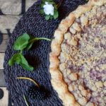 A blackberry orange mint pie on a placemat garnished with orange zest, mint leaves, and flowers