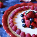 A whole cream cheese pie with strawberry, raspberry, and blueberry garnish and American flag in the background.