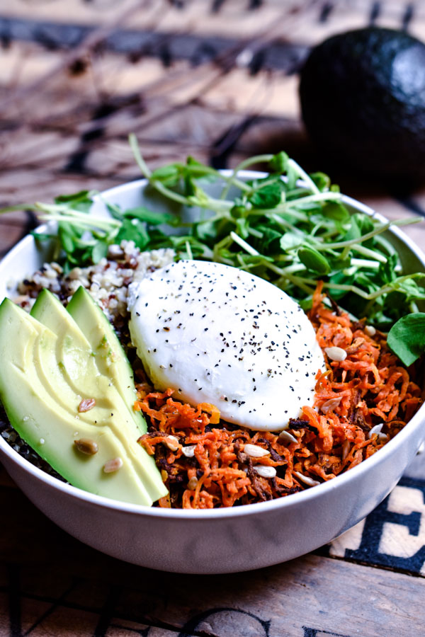 A sweet potato hash quinoa, poached egg bowl garnished with avocado, pea shoots and sunflower seeds.
