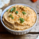 Buffalo Hummus in a bowl garnished with green onions and crackers on the side.