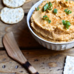 Buffalo Hummus in a bowl garnished with green onions and crackers on the side.