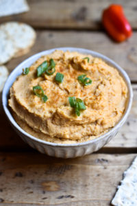 Buffalo Hummus in a bowl garnished with green onions and crackers on the side.