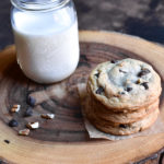 A stack of three chocolate chip cookies next to a glass of milk.