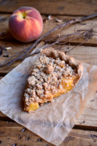 A slice of peach pie with twigs and a peach in the background