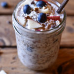 A mason jar of muesli garnished with apple, coconut, and blueberry.