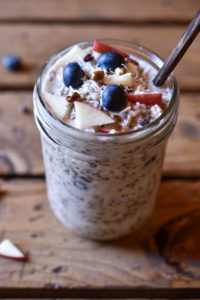 A mason jar of muesli garnished with apple, coconut, and blueberry.
