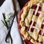 A Rhubarb Pie with a lattice crust and a backdrop of vanilla beans, flowers, and pinecones