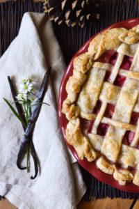 A Rhubarb Pie with a lattice crust and a backdrop of vanilla beans, flowers, and pinecones