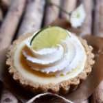 A key lime tarts garnished with fresh whipped cream, lime, and a flower in the background