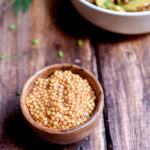 Pickled Mustard Seeds with a bowl of potato salad and dill garnish in the background