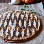 A grilled sautéed vegetable quesadilla with a bell pepper and garlic in the background