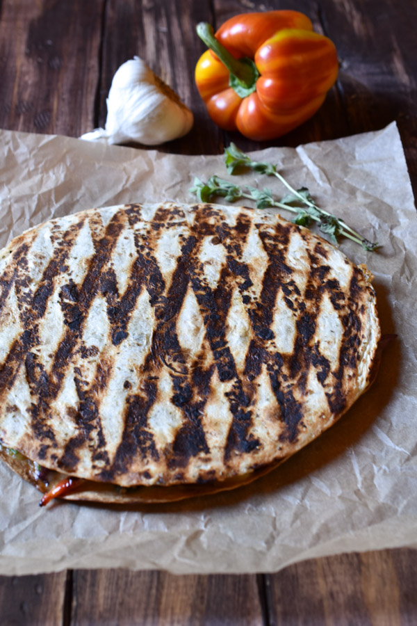 A grilled sautéed vegetable quesadilla with a bell pepper and garlic in the background