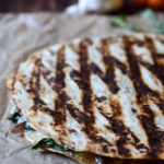 A grilled sautéed vegetable quesadilla with a bell pepper and garlic in the background