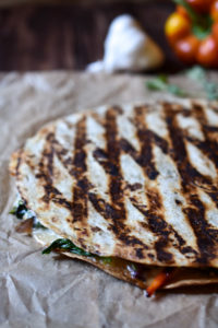 A grilled sautéed vegetable quesadilla with a bell pepper and garlic in the background