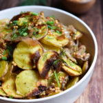 A bowl of roasted potato salad garnished with fresh dill.