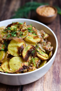 A bowl of roasted potato salad garnished with fresh dill.