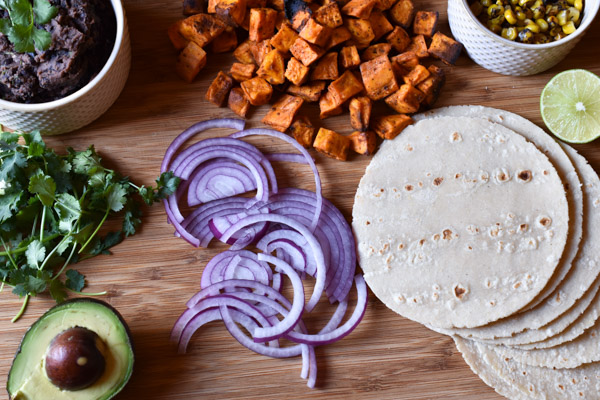 The makings for taco bites: roasted sweet potato and corn, cilantro, avocado, tortillas, lime, and black beans