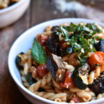 A bowl of Grilled Veggie Pasta with another and shredded parmesan the background