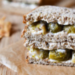 A brussel sprout sandwich on a cutting board with one in the background