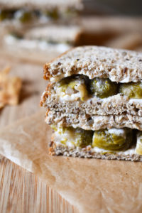 A brussel sprout sandwich on a cutting board with one in the background