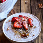 A bowl of Strawberry Pecan Cream of Buckwheat topped with coconut sugar, sliced strawberries, pecans, and chia seeds with a smaller bowl of strawberries in the background.