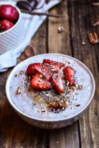 A bowl of Strawberry Pecan Cream of Buckwheat topped with coconut sugar, sliced strawberries, pecans, and chia seeds with a smaller bowl of strawberries in the background.