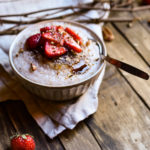 A bowl of Strawberry Pecan Cream of Buckwheat topped with coconut sugar, sliced strawberries, pecans, and chia seeds with a smaller bowl of strawberries in the background.