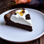 A slice of Fallen Chocolate Cake topped with orange zest whipped cream and chocolate curls