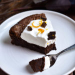 A slice of Fallen Chocolate Cake topped with orange zest whipped cream and chocolate curls