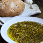 Garlic Herb Bread Oil Dip with sourdough bread in the background.