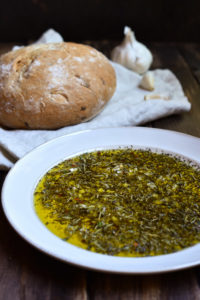 Garlic Herb Bread Oil Dip with sourdough bread in the background.