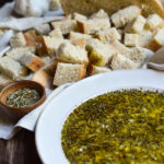 Garlic Herb Bread Oil Dip with sourdough bread in the background.