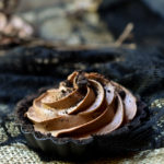 A chocolate mousse tart with cob web decorations in the background.