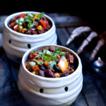 Two bowls of vegetable chili in a mummy bowl with a skeleton hand in the background