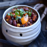 A bowl of vegetable chili in a mummy bowl with a skeleton hand in the background