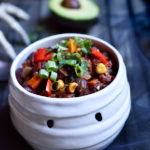 A bowl of vegetable chili in a mummy bowl with a skeleton hand and avocado in the background