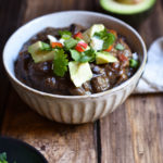 A bowl of Ancho Black Bean Soup with a half avocado and cilantro in the background