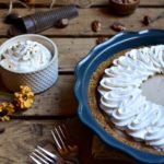 Autumn Spiced Cream Pie with a bowl of fresh whipped cream, nutmeg and a grater, pecans, and burnt orange flowers in the background