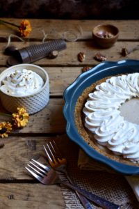 Autumn Spiced Cream Pie with a bowl of fresh whipped cream, nutmeg and a grater, pecans, and burnt orange flowers in the background
