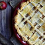 Brandy Apple Pie with apples, a nutmeg and a grater, and cinnamon sticks in the background.