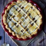 Brandy Apple Pie with apples, dried flowers, and cinnamon sticks in the background.